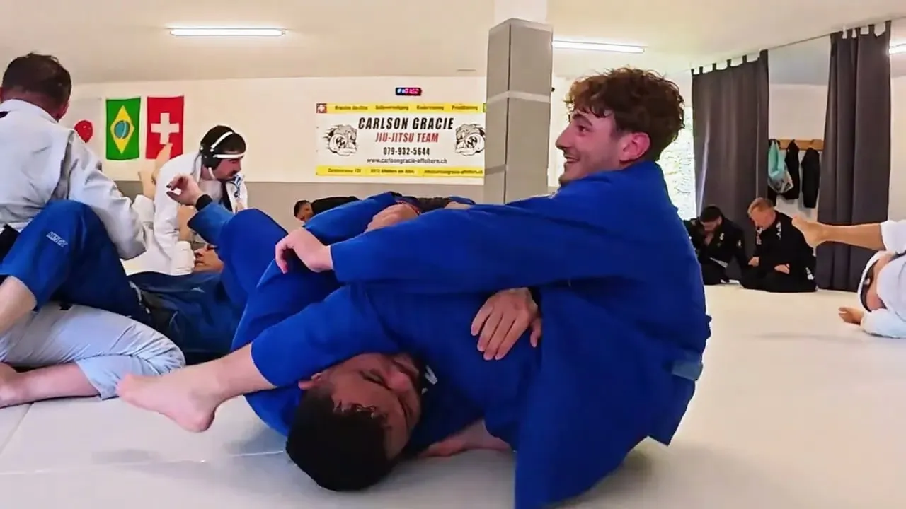 Standbild aus dem Promo-Video: Trainierender im blauen Kimono kontrolliert lachend seinen Partner, dahinter die volle Matte