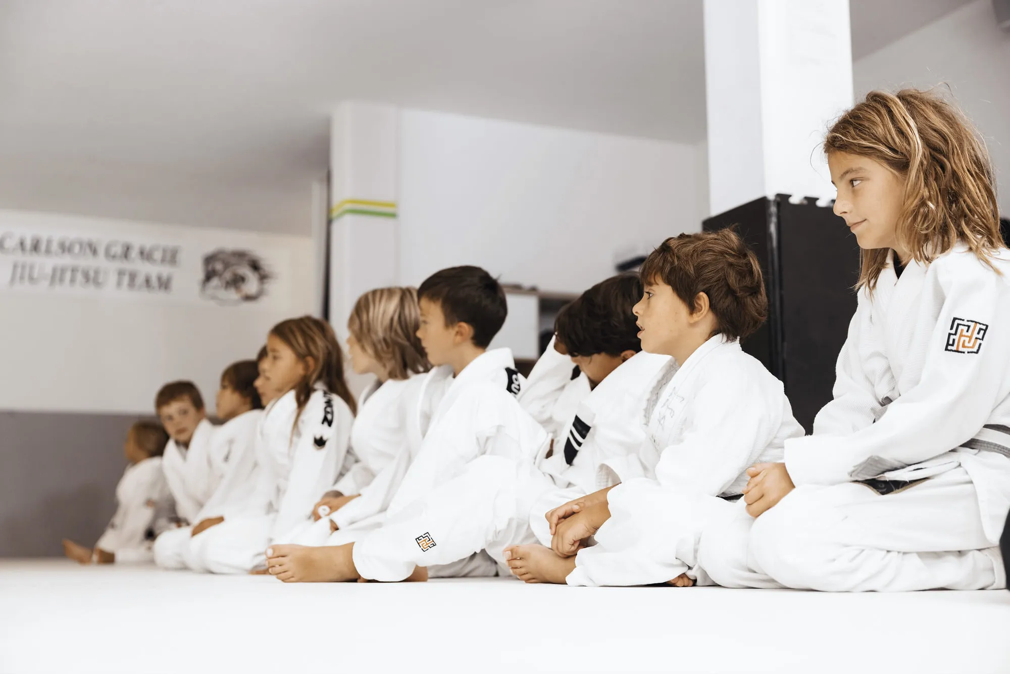 Kindergruppe im weissen Kimono sitzt vor dem Teambanner auf der Matte