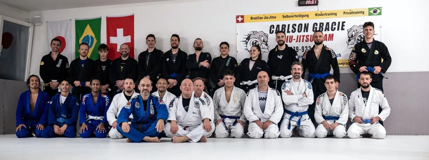 Gruppenbild der Carlson Gracie Academy Affoltern am Albis: rund zwanzig Trainierende aller Gürtelgrade vor dem Teambanner und den Flaggen von Japan, Brasilien und der Schweiz