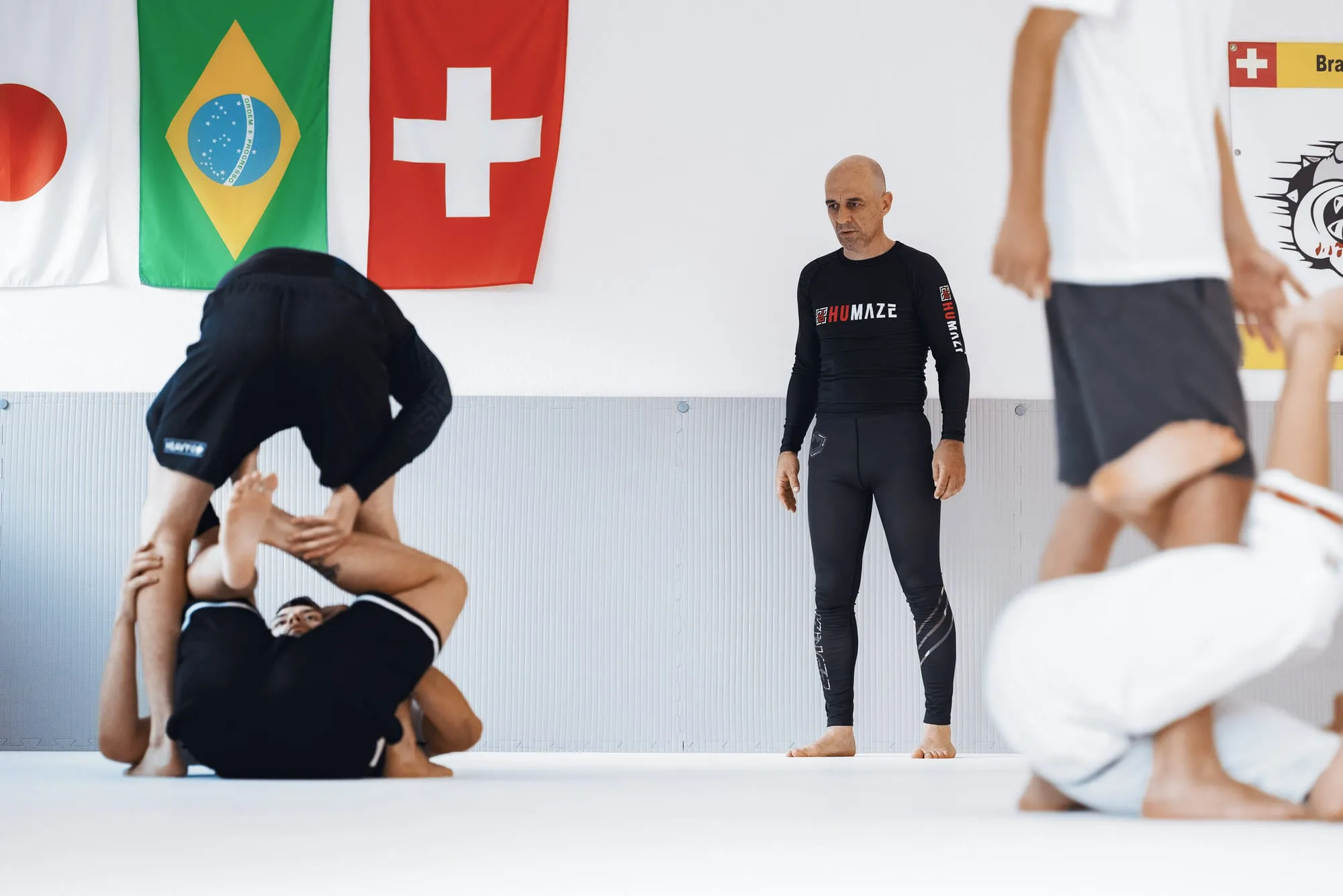 Trainer beobachtet eine Erwachsenengruppe beim Üben, im Hintergrund die Flaggen von Japan, Brasilien und der Schweiz