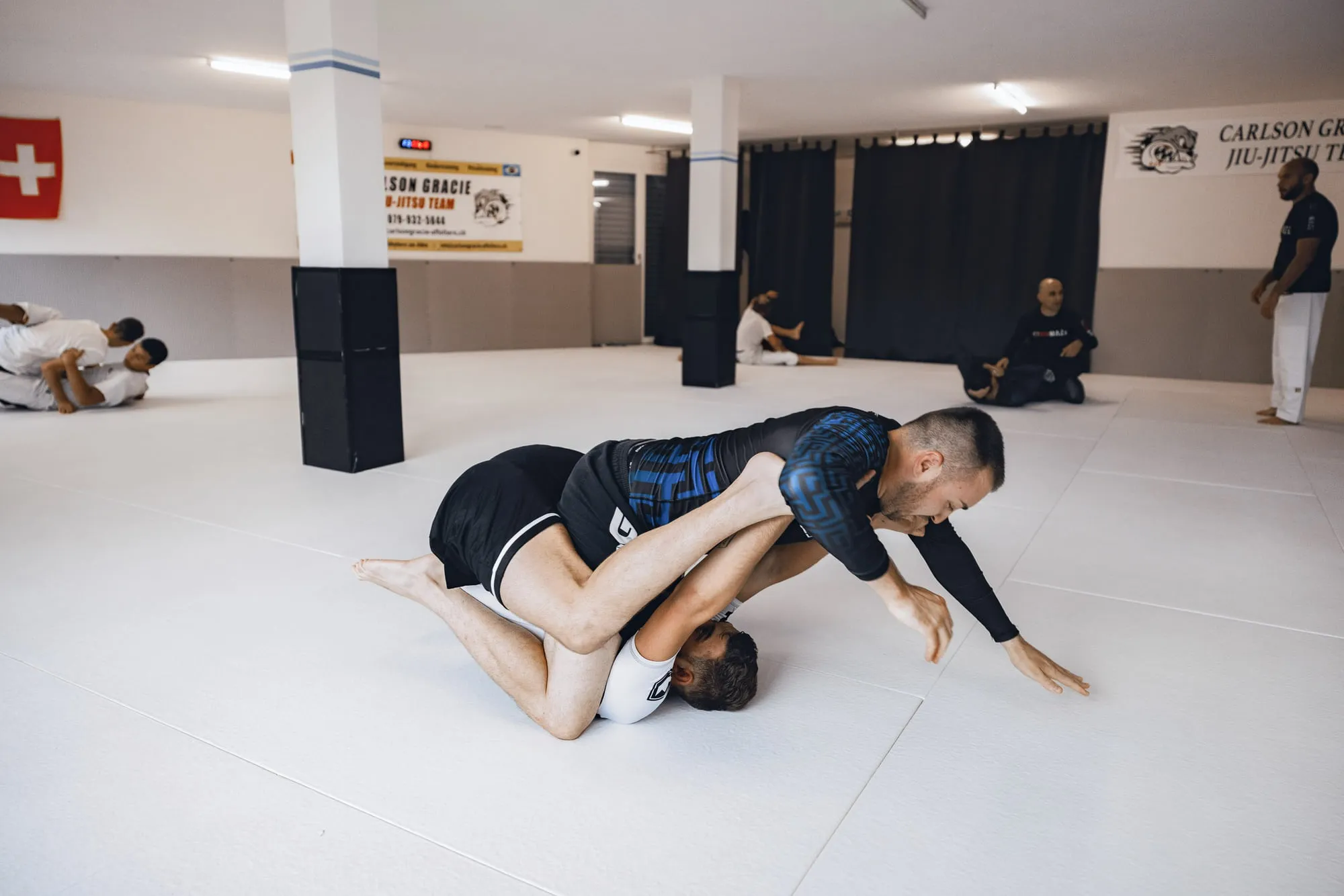 Guard-Pass im No-Gi-Training, im Hintergrund weitere Paare auf der Matte