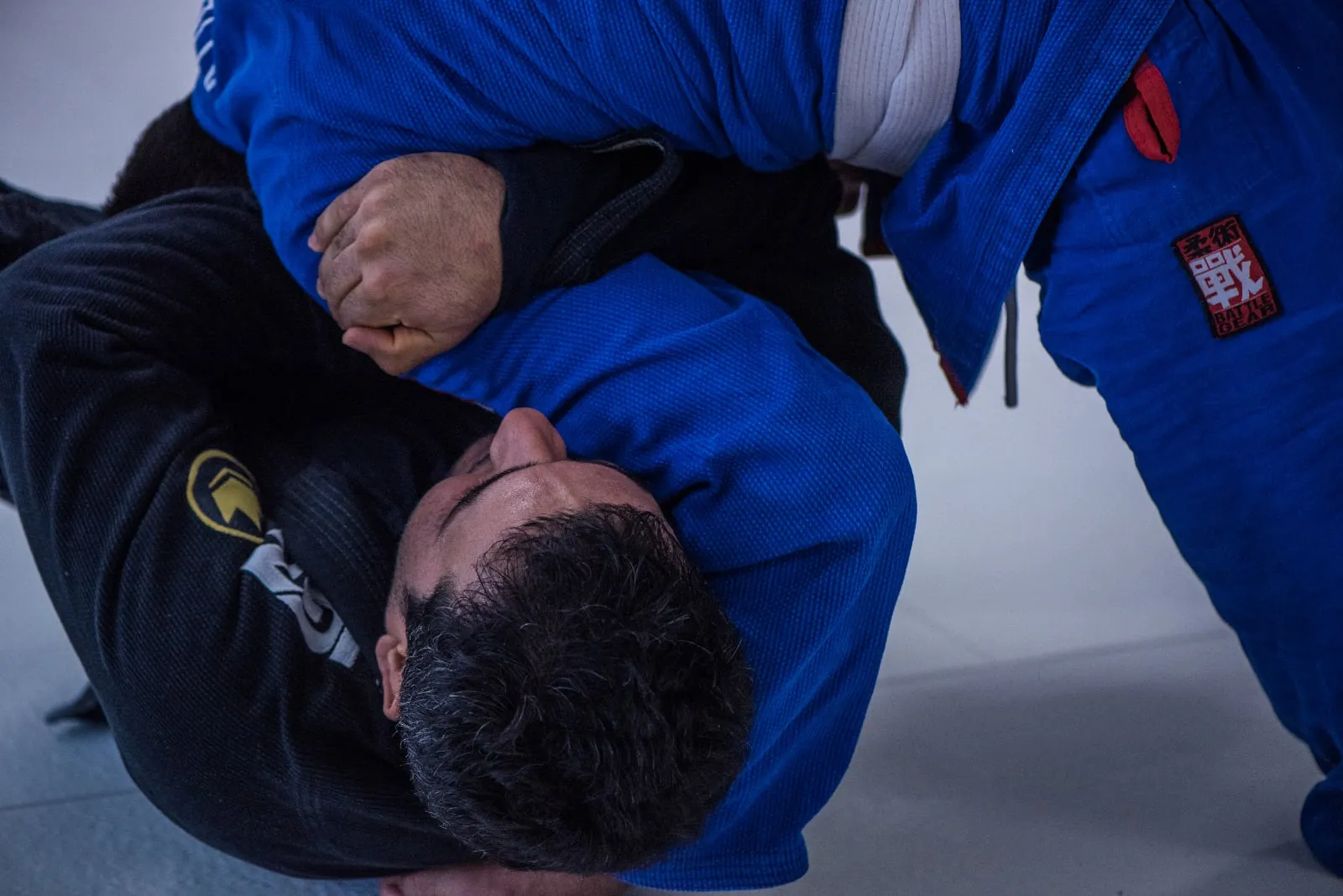 Nahaufnahme von zwei Brazilian-Jiu-Jitsu-Trainierenden im blauen und schwarzen Kimono beim kontrollierten Bodenkampf